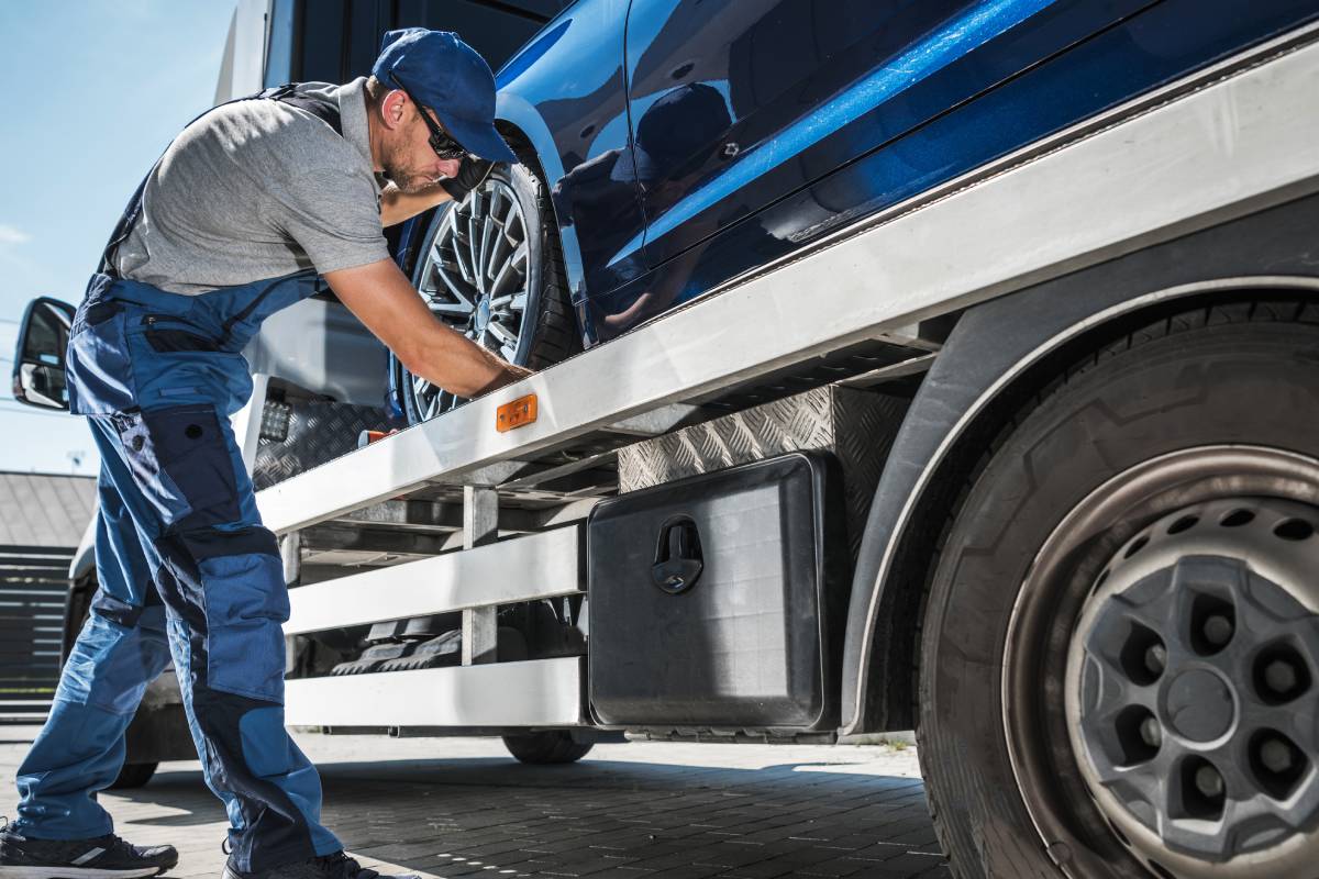 Towing Worker Delivering Brand New Car from Dealer to Client. Caucasian Man Checking the Fastenings to Ensure Safe Transportation on His Tow Truck.